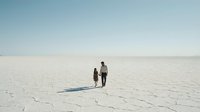 Adult and child walking together across vast white salt flat desert landscape under clear sky, suitable for travel and family concepts.