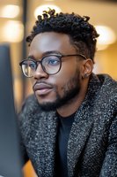 Young African American professional wearing glasses and tweed jacket gazes thoughtfully in modern office setting, conveying confidence and success.
