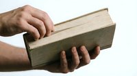 Male hands holding thick vintage book with worn green cover and aged pages on white background for educational and literary projects.