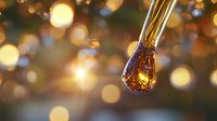 Glowing amber liquid droplet falling with golden bokeh background, macro photography capturing light refraction and luminous effect in motion.