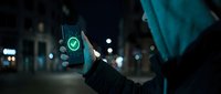 Young adult male of South Asian descent holding smartphone displaying green checkmark symbol at night on urban street, representing mobile app approval, digital verification, and online success for technology and business concepts.