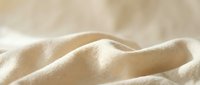 Soft beige fabric with gentle folds and natural lighting creating warm shadows and highlights for textile and interior design projects.