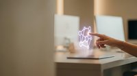 Young woman with medium skin tone interacting with glowing neon purple holographic star symbol above laptop keyboard in modern office workspace for technology and innovation concepts.