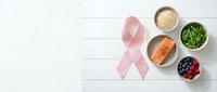 Pink ribbon with healthy foods including salmon, quinoa, spinach and berries on white wooden background for cancer awareness and prevention nutrition.