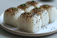 Steamed rice balls topped with black sesame seeds and fresh herbs served on ceramic plate, traditional Asian cuisine preparation for restaurant menu.