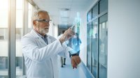 Senior male doctor with glasses and white coat examining medical x-ray in modern hospital corridor for healthcare diagnosis and treatment planning.