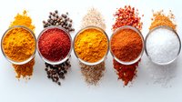 Vibrant aromatic spices and seasonings in white bowls arranged in row on white background, including turmeric, paprika, black peppercorns, cumin and sea salt.