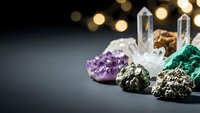 Collection of healing crystals and gemstones including amethyst, quartz points, malachite and pyrite arranged on dark surface with bokeh lights background.