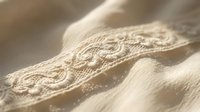 Cream lace trim detail on soft fabric with delicate embroidered pattern, isolated on white background for textile and fashion design projects.