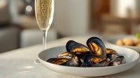 Fresh steamed mussels served on white ceramic plate with champagne glass in soft natural lighting, creating luxurious dining atmosphere.