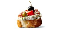 Gourmet bruschetta with cream cheese, prosciutto, olives, cherry tomato and black cherry on toasted baguette slice against white background.