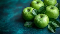 Fresh green apples with water drops and leaves on dark turquoise background. Natural organic fruit composition with moody lighting and copy space.