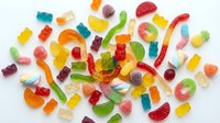 Colorful assorted gummy candies scattered on white background including bears, worms, rings and fruit shapes for sweet treats and confectionery designs.