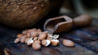 Rustic wooden scoop filled with raw almonds scattered on dark textured surface, natural organic nuts for healthy snacking and cooking ingredients.