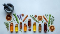 Essential oils collection with herbs spices and dried orange slices arranged on white background for aromatherapy wellness and natural medicine applications.