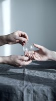 Hands passing crystal clear glass sphere between palms in minimalist setting with soft natural lighting and neutral background for mindfulness concepts.