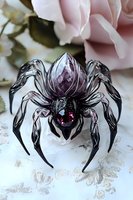 Crystal spider brooch with purple gemstone on delicate lace background with soft pink roses, showcasing intricate metalwork and gothic jewelry design.
