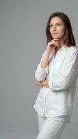 Thoughtful young Caucasian businesswoman in white shirt looking up with hand on chin in contemplative pose against gray studio background.