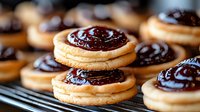 Homemade sandwich cookies with dark chocolate cream filling arranged on cooling rack, close up view of fresh baked sweet treats with glossy topping.