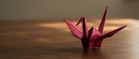 Pink origami crane on wooden surface with soft natural lighting creating peaceful zen atmosphere for meditation and mindfulness practices.