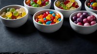 Colorful assorted candies and sweets in white ceramic bowls on dark slate background for confectionery business and dessert menu design.