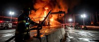 Firefighters battle intense warehouse blaze at night with emergency vehicles and dramatic flames illuminating industrial scene for safety training materials.