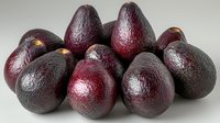 Fresh ripe dark purple avocados with textured skin arranged in group on light background, healthy organic produce for nutritious eating and cooking.