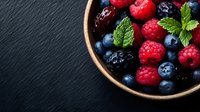 Fresh mixed berries with mint leaves in ceramic bowl on dark slate background, overhead view of raspberries, blueberries and blackberries for healthy eating concept.
