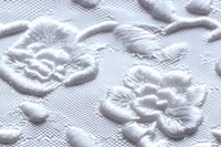 Delicate white embossed floral pattern on textured fabric surface creates elegant relief design with raised flowers and leaves, showing subtle shadows and depth.