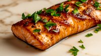 Glazed salmon fillet with caramelized surface, fresh parsley garnish, and green onions on marble background. Suitable for food blogs, restaurant menus, and culinary publications.