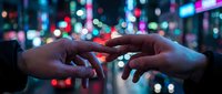 Two hands touching fingertips against blurred neon city lights, symbolizing connection, technology, and digital communication in urban environment.
