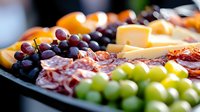 Fresh charcuterie board with assorted meats, cheese cubes, purple and green grapes, and citrus fruits arranged on dark slate platter for entertaining and events.