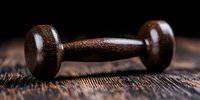 Vintage wooden dumbbell on rustic wooden surface with dramatic lighting and shallow depth of field, showcasing antique fitness equipment for sports history concept.