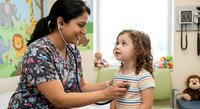 Female pediatric nurse with stethoscope examining young Caucasian girl patient in colorful medical office. Healthcare professional checkup consultation.