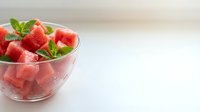 Diced watermelon cubes in clear glass bowl with fresh mint leaves on white surface, ready for summer desserts and healthy eating content.