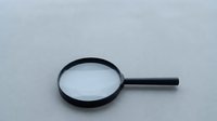 Magnifying glass with black frame and handle on neutral gray background, useful for research, education, inspection, and detective work.