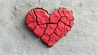 Red cracked heart shape on concrete background symbolizing broken love, heartbreak, and emotional pain. Artistic metaphor for relationship problems and divorce.