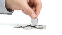 Caucasian male hand dropping silver coin onto pile of coins against white background, representing savings, investment, and financial growth.