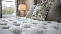 Luxury mattress surface with tufted pattern and decorative floral pillows in modern bedroom interior, soft natural lighting through window creates cozy atmosphere.