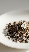Mixed peppercorns and coarse sea salt crystals on white plate creating aromatic seasoning blend for gourmet cooking and culinary applications.