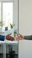 Business handshake between diverse professionals in modern office setting with natural light and plants creating welcoming corporate atmosphere.