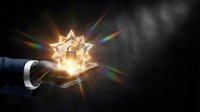 Businessman hand holding glowing star with rainbow light rays on dark background, representing success, achievement, innovation and business excellence concept.