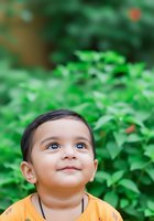 Toddler boy with dark hair and light skin wearing yellow shirt gazes upward against lush green foliage background. Suitable for parenting, childhood development, and nature-themed content.