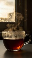 Steaming hot tea in a glass cup on a dark table by a rain-covered window, creating a cozy autumn mood with warm golden light.