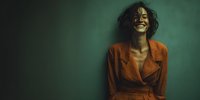 Happy African American woman in orange blazer laughing against green wall. Professional portrait for business, lifestyle and wellness content.