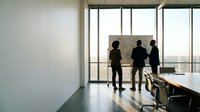 Business professionals discussing strategy at whiteboard in modern office conference room with city view windows for corporate presentations.