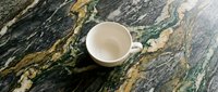 Empty white ceramic cup on dark marble surface with gold veining, overhead view. Suitable for beverage, kitchen, and tableware design projects.