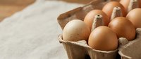Fresh brown and white chicken eggs in eco-friendly cardboard carton on rustic wooden table surface for organic farm cooking and baking ingredients.