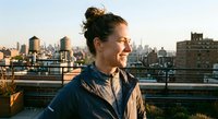Young woman enjoying golden hour sunset on urban rooftop with city skyline background. Casual lifestyle portrait for wellness and mindfulness content.