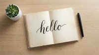 Open vintage notebook with hello in calligraphy script on wooden desk, pen and succulent plant beside it, warm tones.